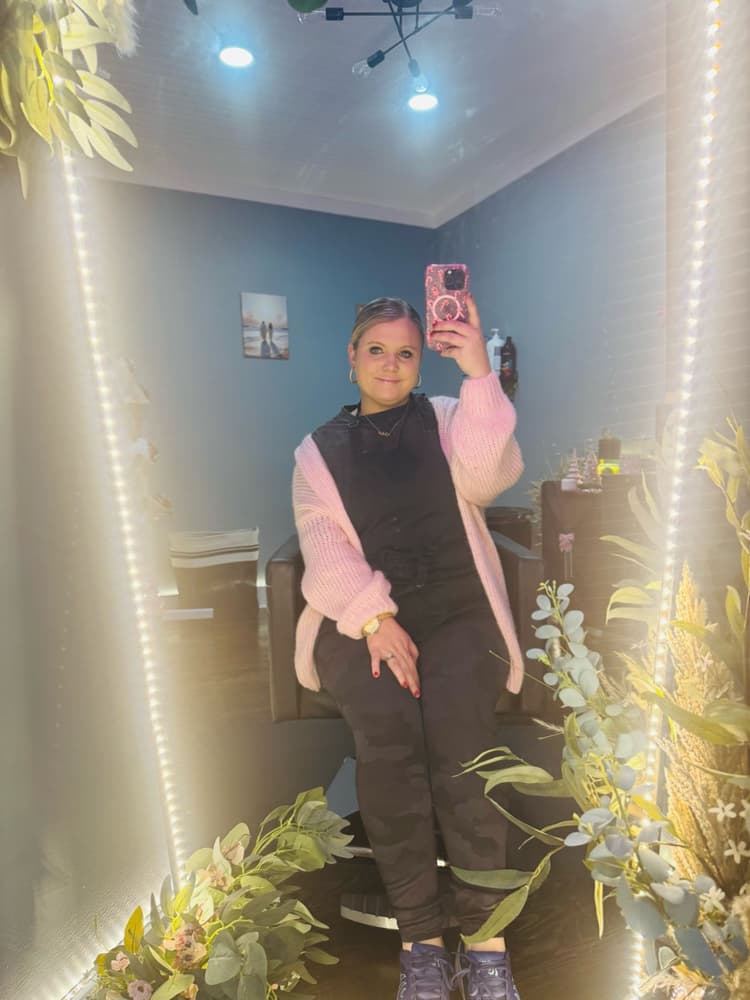 Brooke Holland in her salon wearing a pink cardigan, taken in a mirror.